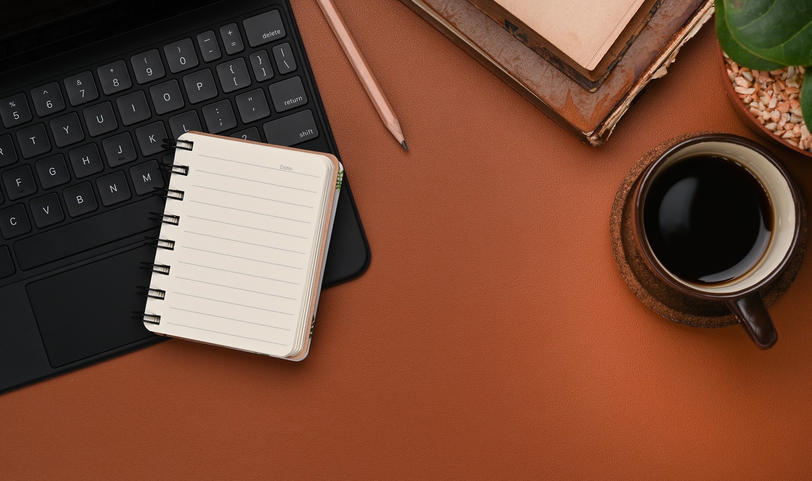 Overhead shot of contemporary workplace with coffee cup, notebook, keyboard and copy space brown leather.