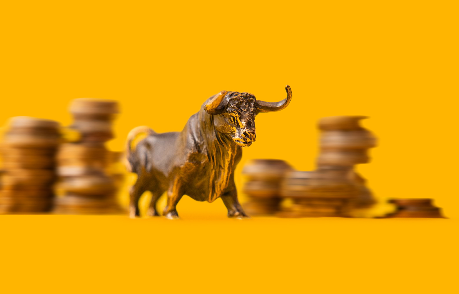 A bull figurine in front of stacked coins on a yellow background