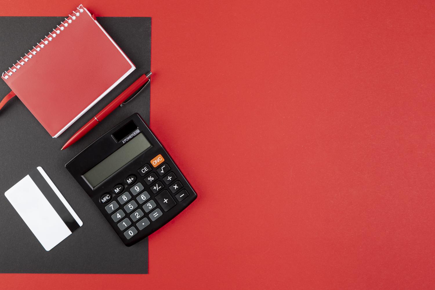 Calculator, credit card, and a writing pad on red background